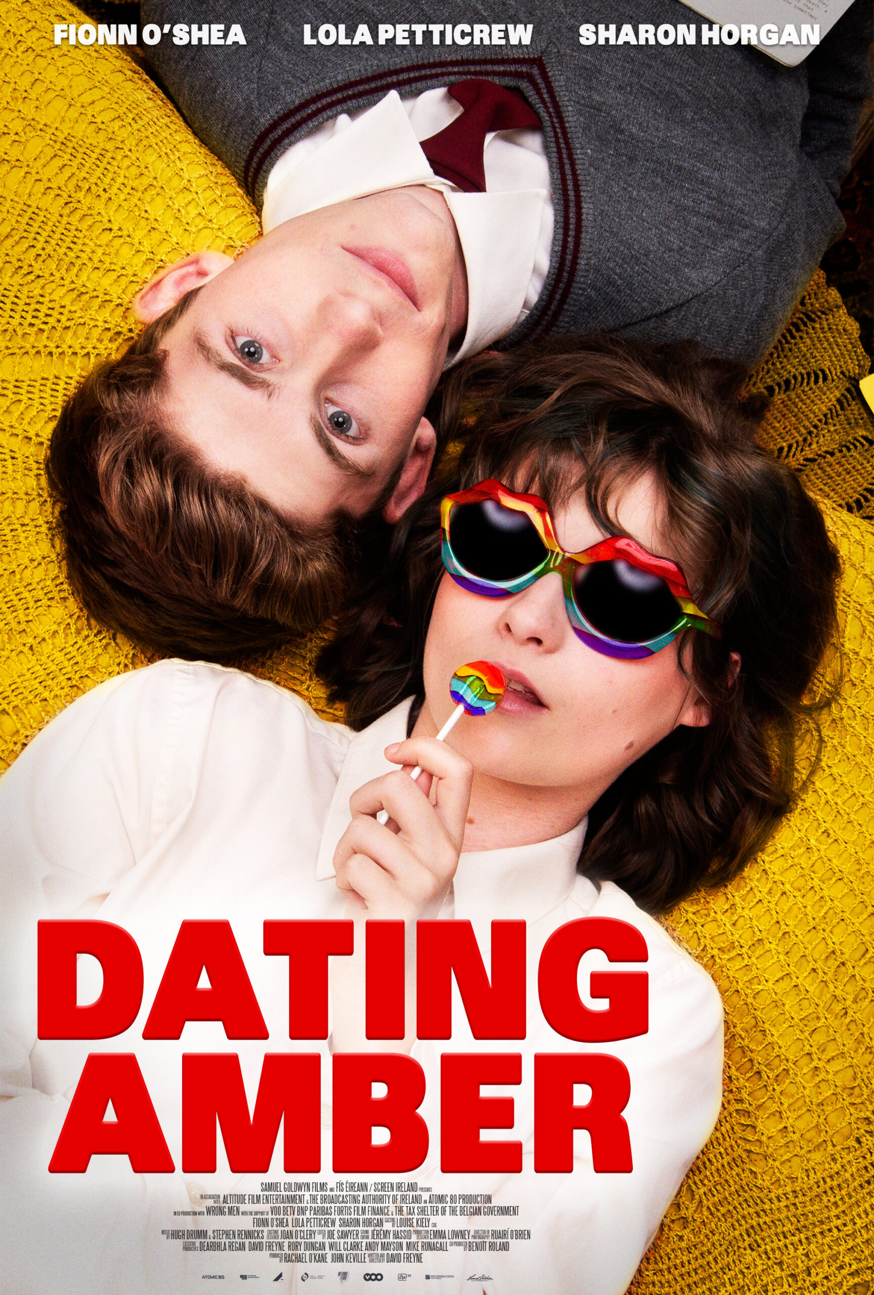 movie poster featuring a young white man and a young white woman wearing sunglasses laying on a yellow floor so their heads on each other shoulders