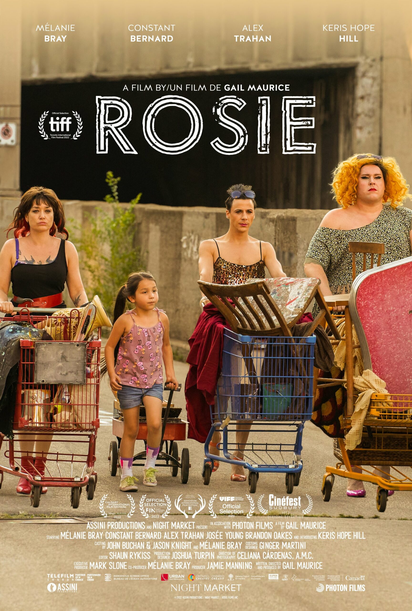 Four figures, three adults and one child, walk down a street pushing grocery carts, with the word ROSIE on a sign behind them.