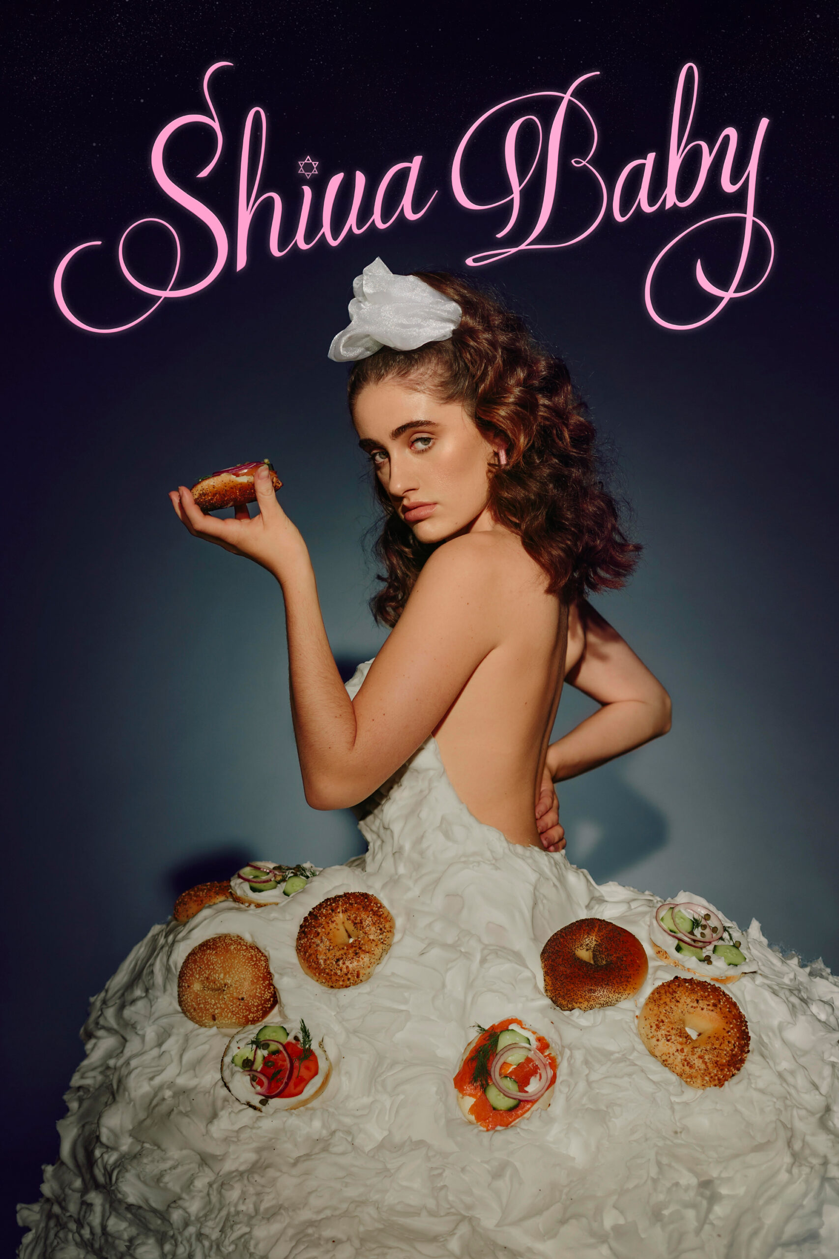 A young woman with brown curly hair wears a white puffy dress covered in bagels
